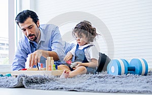 Caucasian handsome father taking care, playing toys with his little cute daughter on floor in cozy living room at home after work