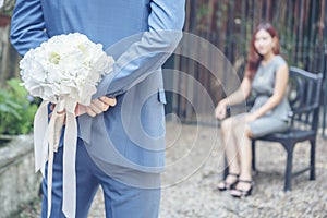 Caucasian handsome man giving flowers to asian girlfriend asking for proposing to marry him at green park. Couple lover on
