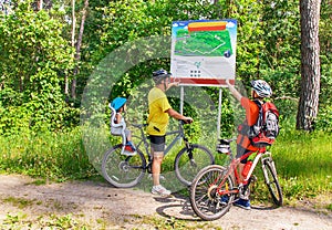 Caucasian happy family with bicycles is near map in the park.