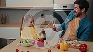 Caucasian happy family having fun fooling around at kitchen father with daughter fighting with spoons cooking daddy with