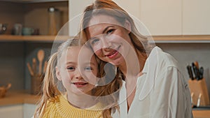 Caucasian happy family at kitchen. Close up smiling child daughter cuddling mom look at camera. Adult single mother