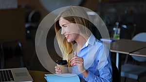 Caucasian happy female waving hand chatting online on video call on laptop in restaurant. Close up. Young woman with cup