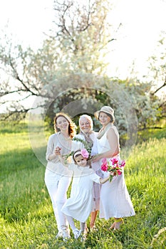 Caucasian happy granny in white dress with daughter and granddaughters outdoors.