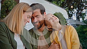 Caucasian happy loving family talking outdoors dad touching nose of little daughter child girl and mother wife kissing