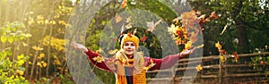 Caucasian happy smiling woman girl in warm yellow scarf and hat throwing autumn fall orange red leaves in park forest outdoor.