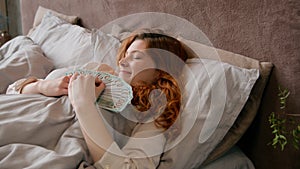 Caucasian happy woman sleeping in bed in luxury vacation with money rich wealthy girl businesswoman holding banknotes