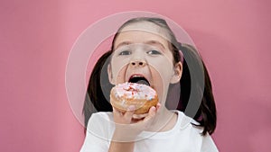 Caucasian healthy girl with ponytails eats donut opening mouth wide, healthy organic homemade food. Pink background.