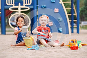 Caucasian and hispanic latin babies children sitting in sandbox playing with plastic colorful toys