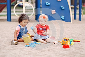 Caucasian and hispanic latin babies children sitting in sandbox playing with plastic colorful toys