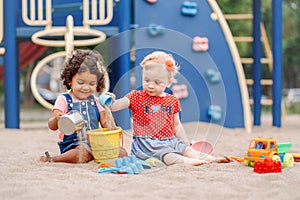 Caucasian and hispanic latin babies children sitting in sandbox playing with plastic colorful toys