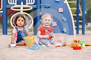 Caucasian and hispanic latin babies children sitting in sandbox playing with plastic colorful toys