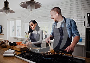 Caucasian husband and wife cooking together in the kitchen, smiling and laughing