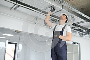 Caucasian HVAC Technician Worker in His 40s Testing Newly Installed Warehouse Ventilation System. Commercial Heating