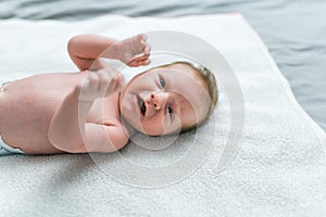 Caucasian infant boy wearing diaper lying on his back on blanket on floor fidgeting ready to get changed. Changing