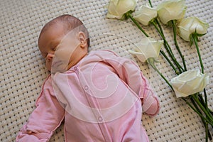 Caucasian infant girl in pink bodysuit lying on her back with roses flowers on the bed at home