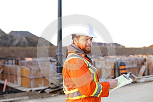 Caucasian inspector in orange workwear with blueprints on construction site.