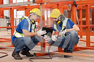 Caucasian iron welding workers with tablet in front of the red steel structure