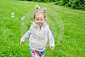 Caucasian kid happy running in a summer park with soap bubbles