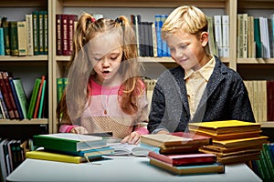 caucasian kids reading book together while sitting at table in library