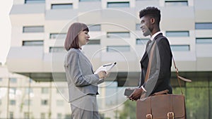 Caucasian lady welcomes African American male colleague, shaking hands near office building