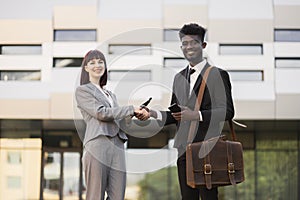 Caucasian lady welcomes African American male colleague, shaking hands near office building