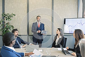 caucasian leader with tablet in hand coaching interested business people, giving educational workshop presentation in Concentrated