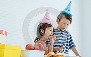 Caucasian little adorable sibling boy and girl celebrating birthday party with fruits, gifts or presents and foods while playing