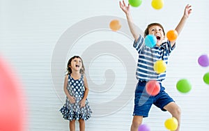 Caucasian little adorable sibling boy and girl laughing, screaming, celebrating birthday party, playing colorful balls together