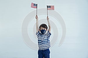 A Caucasian little boy wear mask holding american flag in his two hands