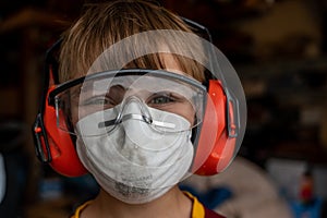 Caucasian little boy wearing a protective dust mask, safety glasses, and hearing protection