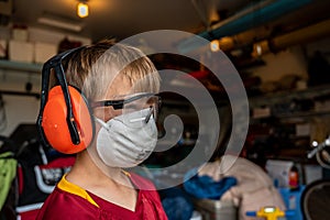 Caucasian little boy wearing a protective dust mask, safety glasses, and hearing protection