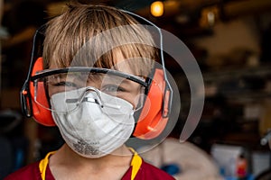 Caucasian little boy wearing a protective dust mask, safety glasses, and hearing protection