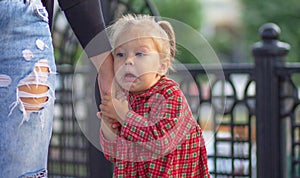 Caucasian little girl of 2 years with scared face holding hand of mother in summertime