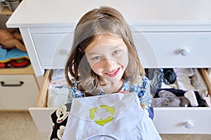 Caucasian little girl in a blue dress happily organizing her clothes for donation and reusing