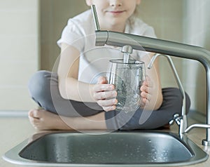 Caucasian little girl drinking from water tap or faucet in kitchen. Pouring fresh drink. Healthy lifestyle. Water quality check