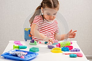 Caucasian little girl enthusiastically plays with plasticine, play dough on white table at home, children`s creativity