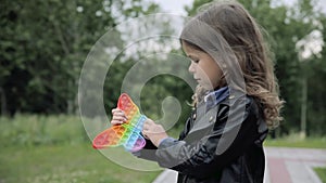 Caucasian little girl playing with pop it silicone squishy trendy toy, pressing on colorful rainbow sensory soft bubbles