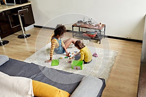 Caucasian little girl spending time with african american baby sitter. They are playing with construction toys set
