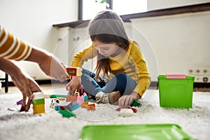 Caucasian little girl spending time with african american baby sitter, playing with construction toys set, sitting on