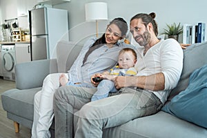 Caucasian loving family watch movie together in living room at home. New marriage couple man and woman sit with young baby boy on