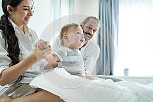 Caucasian loving parents play with baby boy child on bed in bedroom. Happy family, attractive beautiful young couple dad and mom