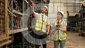 Caucasian male and Asian female work colleague in safety uniform and helmet using a tablet to check automotive spare parts stock s