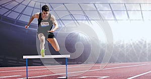 Caucasian male athlete jumping over a hurdle against sports field in background