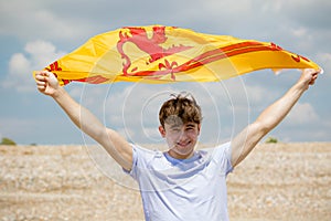 Caucasian male on a beach holding a Lion Rampant of Scotland flag