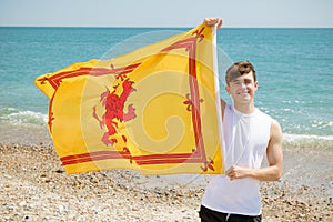 Caucasian male on a beach holding a Lion Rampant of Scotland flag