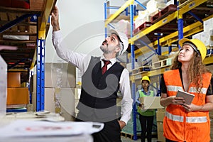 Caucasian male boss is checking for the stock inventory inside warehouse with his female store manager in full safety equipment