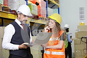 Caucasian male boss is checking for the stock inventory inside warehouse with his female store manager in full safety equipment