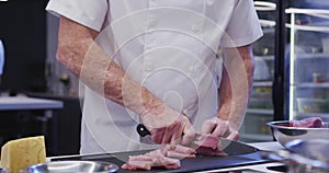 Caucasian male chef wearing chefs whites in a restaurant kitchen slicing meat on a cutting board