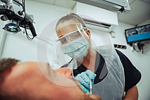 Caucasian male client sitting dentist chair while female nurse operates on broken tooth