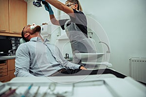 Caucasian male client sitting in doctors chair while female nurse examines wisdom teeth